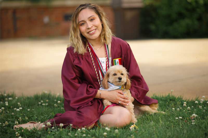 Cinthia Arreola in Commencement Gown seated with dog