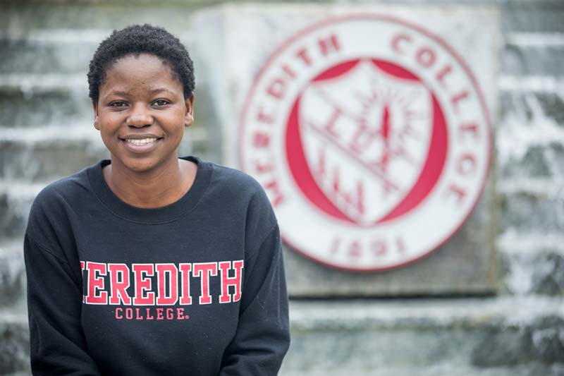 Meredith college student Matilda Odera wearing a Meredith sweatshirt in front of the Meredith College seal